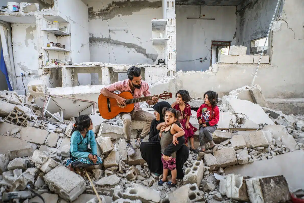 Syrian family sitting in rubble playing the guitar