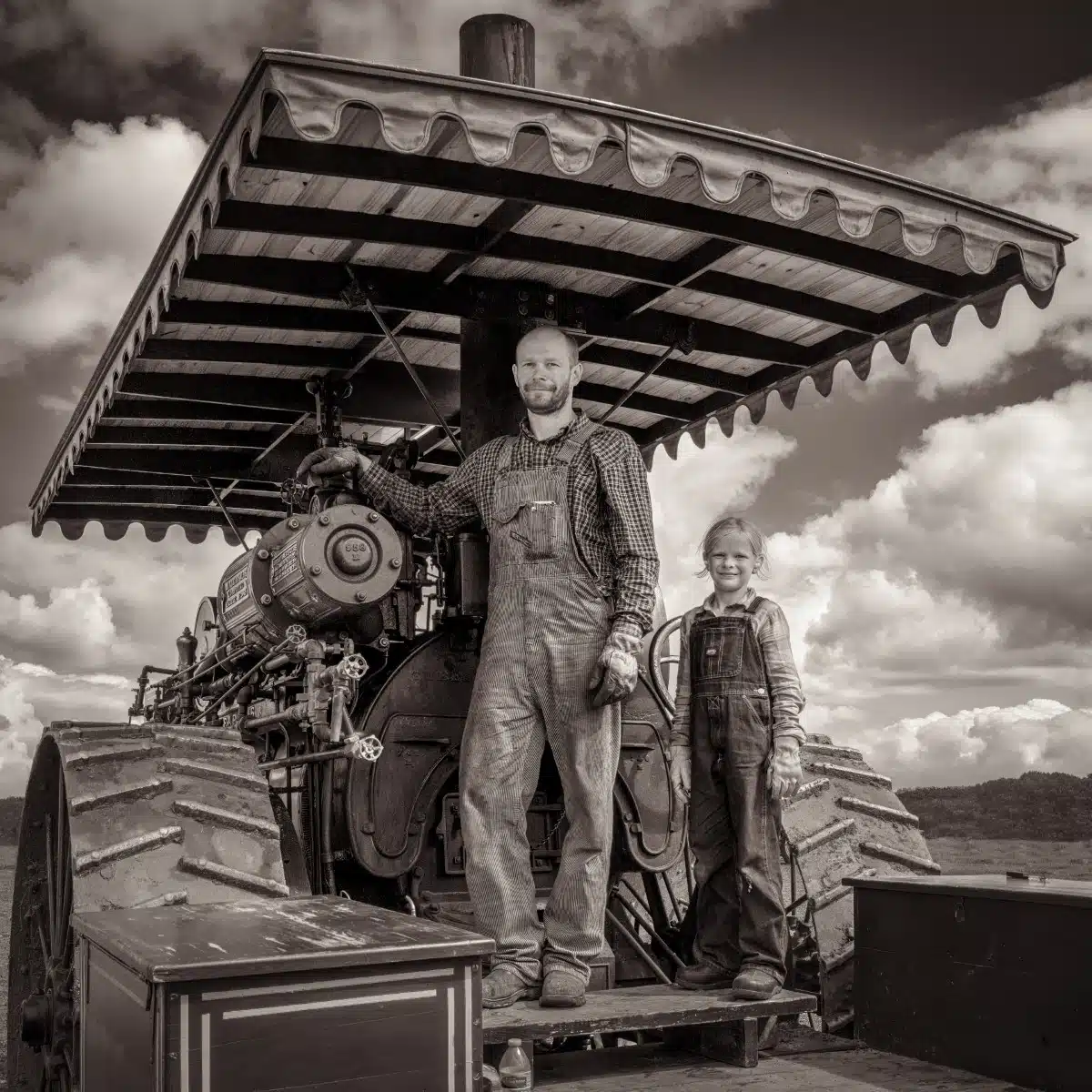Black and white portrait of a man and his daughter on the back of a tractor
