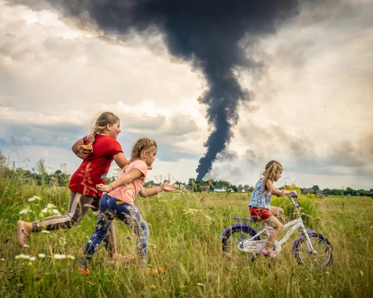 Children in Ukraine playing in a field while smoking from a bombing rises in the background